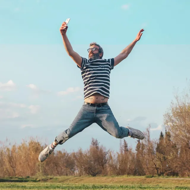 A man jumping in a field with his arms open, phone in hand